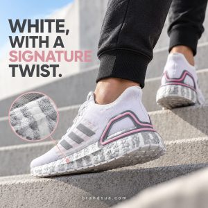 Adidas Ultra Boost David Beckham FX0576 — Cropped adult in charcoal joggers walks bright concrete steps; exact shoe in lateral-rear angle shows grey printed sole and pink heel. Small inset true DB foam pattern, elegant grey/pink headline block. No endorsement claims.